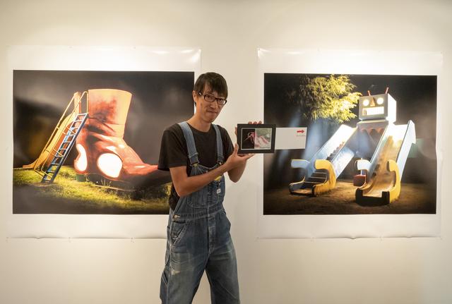 画像: 作者の木藤さん。手にしているのは遊具が昼と夜の姿に変わるなんとも不思議な写真。会場で試せます。