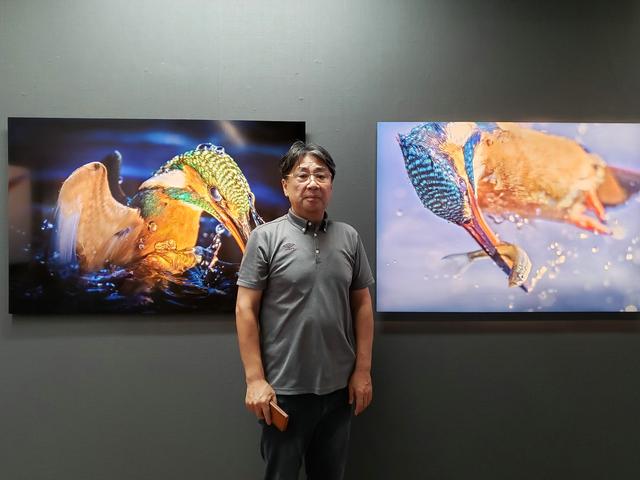 画像: 写真家 小曽納久男さん。翡翠が一瞬一瞬に魅せる美しい形と色を写し撮ることで、野生が生きる力と躍動を感じてもらうことができればと、作品の発表に至ったそうです。