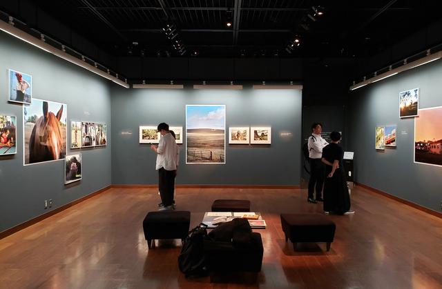 画像: 展示風景。写真展には、初日から多くの方々が訪れ、皆さんが、展示作品を撮影されたり、七咲さんと談笑されたり、作品集などに目を通しながら楽しまれている様子が印象的でした。