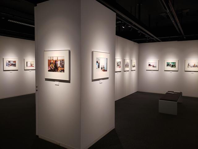 画像: はじめて写真展に足ばれる方へ向けて、本展を鑑賞するポイントを伺ってみると「写真に写っている情報、例えば部屋にベッドが置かれている方だと定住するつもりかな、とかマットだけだと、どうなんだろうと思ったり。ほとんど家具を置かず、いつでもこの町から出いける雰囲気の方もいるので。そういう視点で鑑賞されても面白いと思います。そしてやっぱり“色”の面白さもあると思います」と木村さん。
