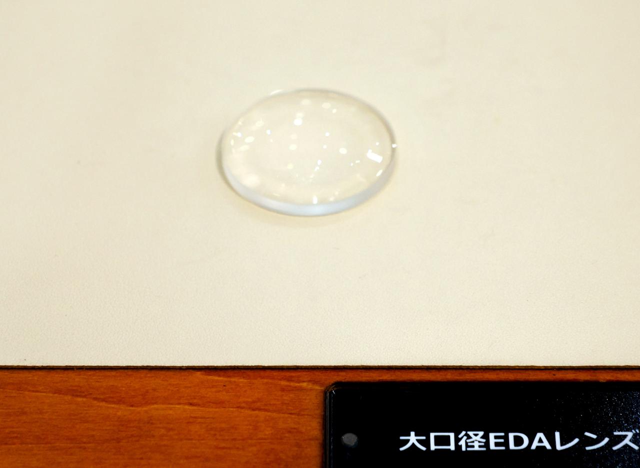 画像: 低分散ガラスに非球面加工が施されたEDAレンズ。レンズ面に映る照明の形から高い強度の非球面形状がわかる。