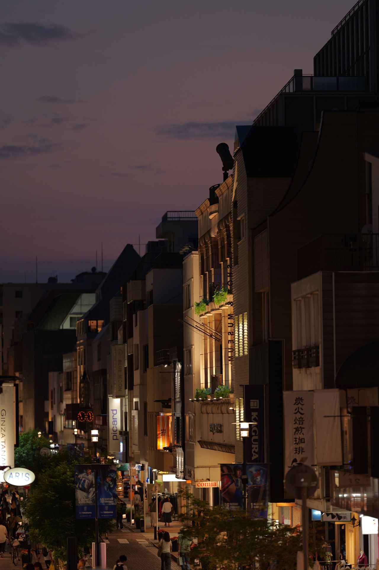 画像: F1.4の明るさを活かして夕暮れの街を手持ち撮影。なかなかいい雰囲気に写っているけど、こんな遠距離でも被写界深度はきわめて浅くてビックリするほど。けれど切れ味がよく、その前後の描写も素直なので、とても自然な立体感が楽しめる。小さなサイズで見てると気付かないけど。 ■絞りF1.4 1/160秒 マイナス1.66露出補正 ISO400