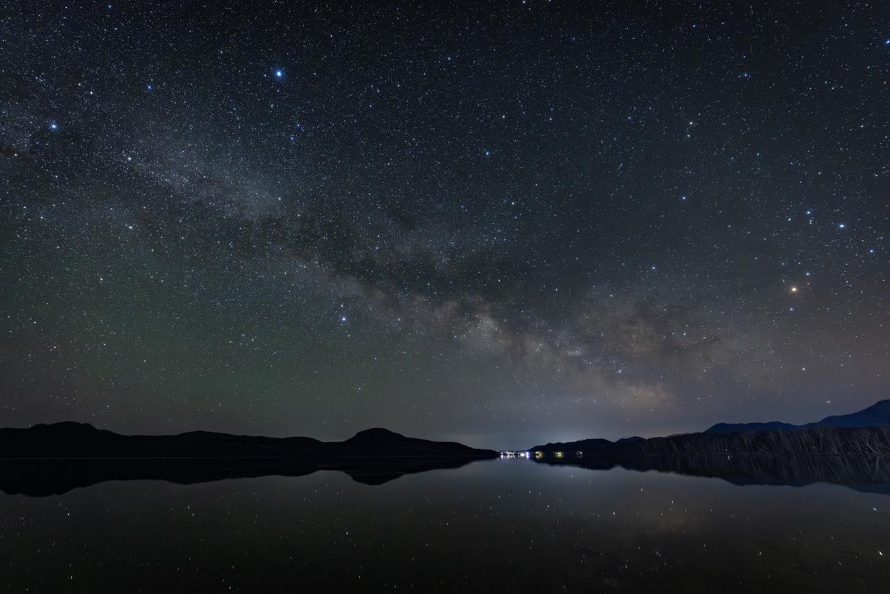 画像: 14㎜という画角は、星景写真専門の方々にとって一番使用頻度の高いレンズだと思う。何故なら、一番人気である夏の天の川が横位置で画面全体に入れ込む事ができるからだ。深夜2時南東の空にさそり座が登り始め、夏の大三角形（ベガ・アルタイル・デネブ）が出揃う。無風の湖面には星達が微かに写り込む。天と地が一体になった荘厳な原風景を再現可能な唯一無二のレンズだと確信する。 ■絞りF1.4　8秒　ISO4000　WB:3400K　※屈斜路湖