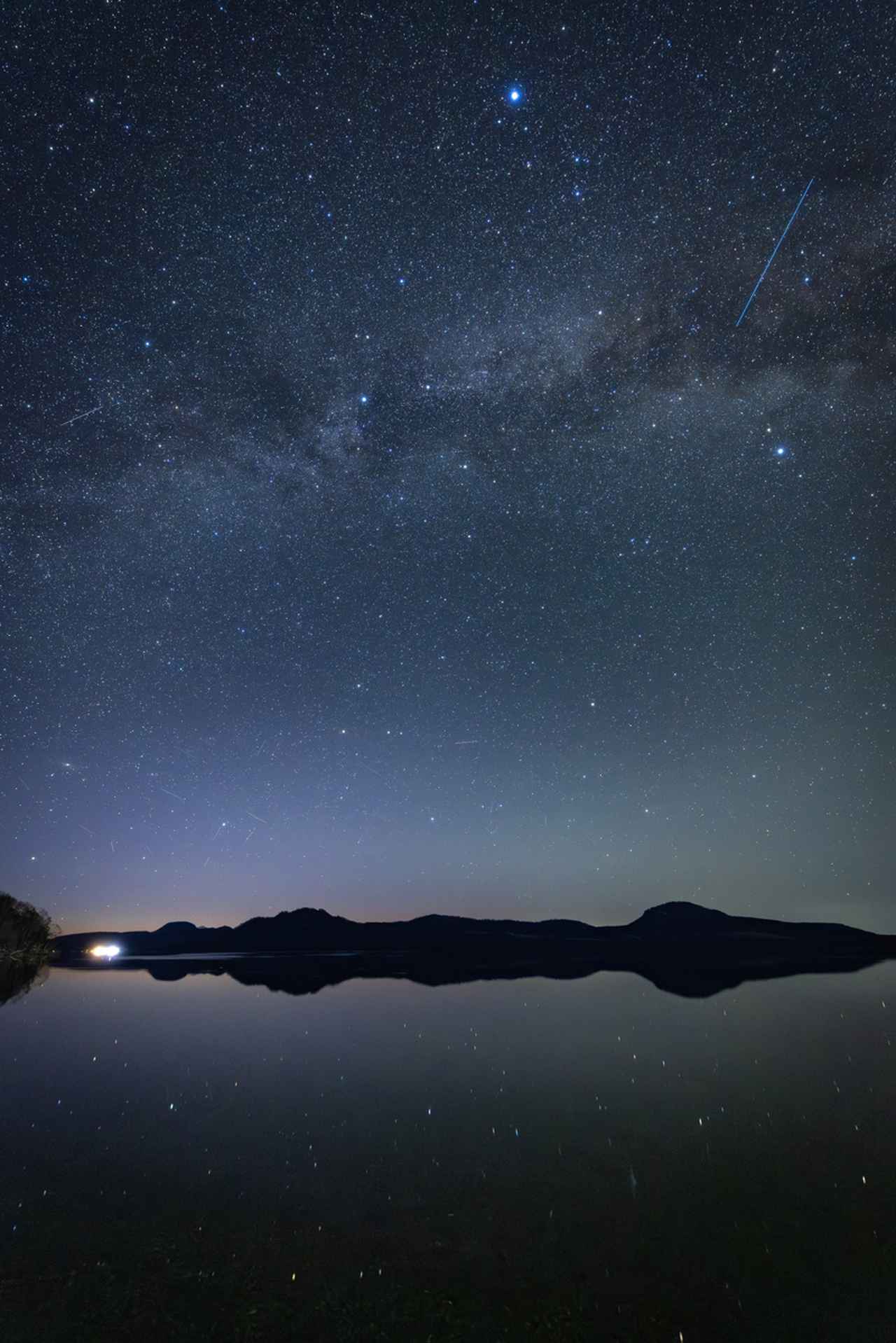 画像: 夜明け前の午前3時過ぎ、夏の天の川が天頂に昇り、南東の空が微かに茜色に染まりはじめた。新型レンズは色収差も歪みも皆無で、解像度も申し分ない。長年明るい広角レンズが無かったキヤノンは、RFレンズになりユーザーが求めているレンズを続々と開発して発売してくれる。EF時代より小型軽量になり撮影レスポンスが明らかに向上した。（画面左下の暁の低空に、4月中旬に地球に接近中の、C2025R3パンスターズ彗星が微かに尾を引いて写り込んでいる） ■絞りF1.4　8秒　ISO4000　WB:3600K　※屈斜路湖