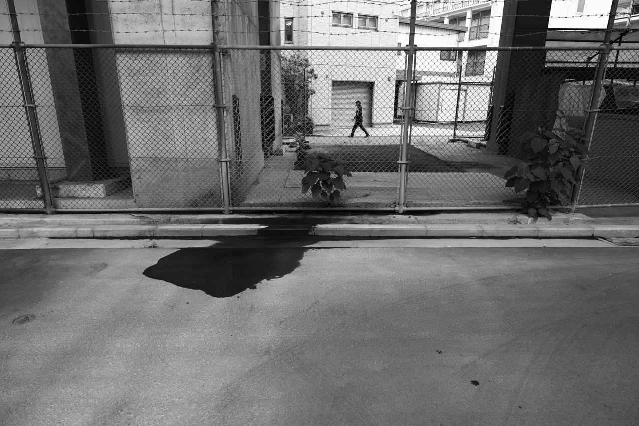 画像: テレ側で路面の水の痕を撮ろうと思ってたら通り過ぎる人がいたので、路線変更してワイド端でパチリ。従来のパワーズームだと諦めていたと思うけれども、本レンズなら手動ズームの速度（時間）感覚で間に合っちゃうのでチャレンジしたら余裕を持って成功しました、の1枚。 ■20mm時　絞りF4.0　1/160秒　マイナス0.7露出補正　ISO100