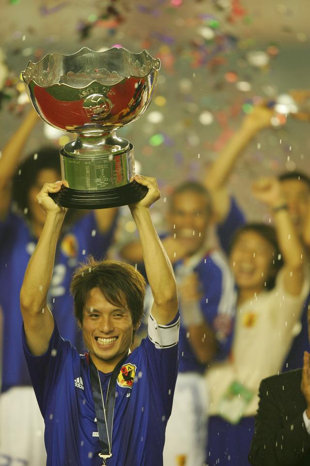 画像: 日本の選手たちの水のシャワーが舞う中、優勝カップを高々と掲げる宮本。この後にジーコ監督にカップを渡そうとした宮本に、指揮官は「それは君たちのものだ」と答え、自らは掲げなかった(写真◎BBM)
