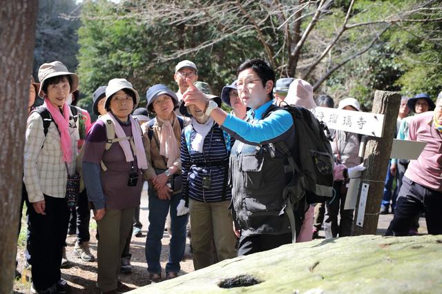 画像: 岩の中央に穴が掘られた「唐臼の壺」にて北尻ガイドの解説に耳を傾ける旅仲間