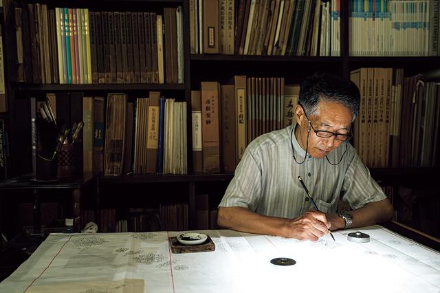 画像: 正倉院由来の鏡裏文（きょうりもん）から想起した原寸図案を光で透かしながら、反物に写す小倉貞右。