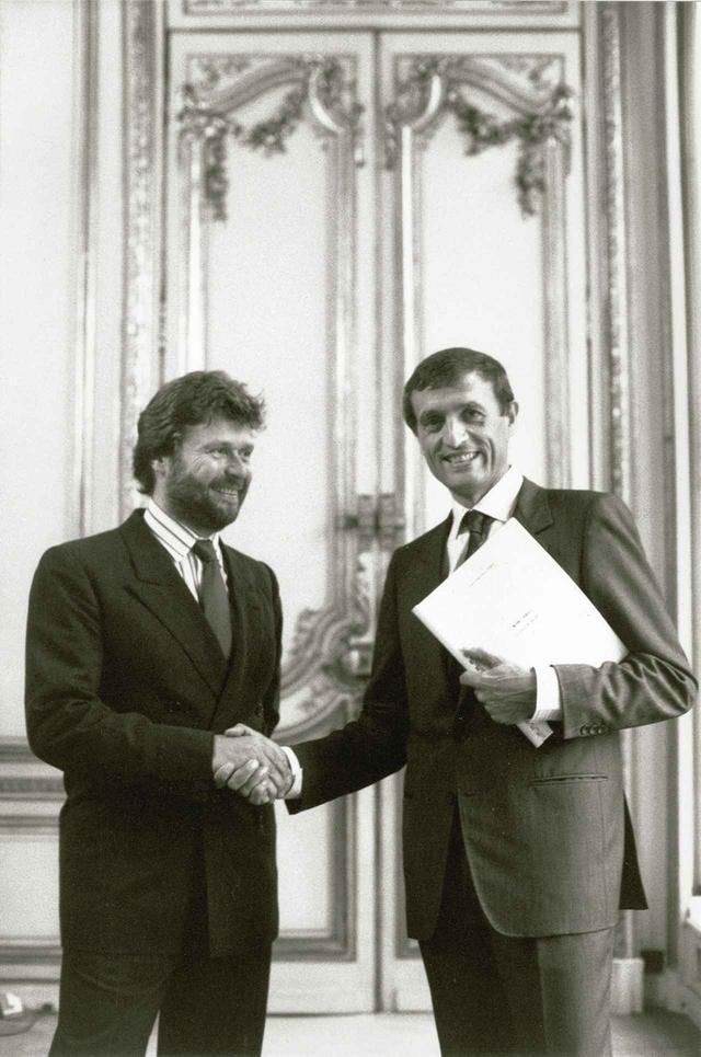 画像: 1986年、ジャック・シラク首相内閣の文化大臣、フランソワ・レオタールに企業のメセナ活動に関する報告書を渡すカルティエのプレジデント、アラン=ドミニク・ペラン(写真左)。この翌年、企業によるスポンサー契約を可能にするレオタール法が成立した。 © SBJ / ADAGP, PARIS, 2024 PHOTOGRAPHER © DOMINIQUE FAGET / AFP