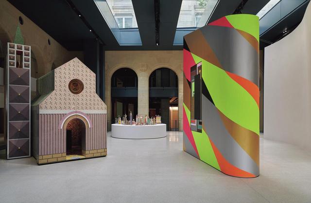 画像: 開館記念展『エクスポジション ジェネラル』の展示風景。正面エントランスを入って最初に展示されている建築作品。小さな教会建築や未来都市の模型が並置されている。右端の色鮮やかな立体作品《OMG!》は2014年、イタリアの建築家アレッサンドロ・メンディーニによってアーティストのピーター・ハリーの抽象画《Code Warrior》をかけるための壁として制作された。 ©MARC DOMAGE