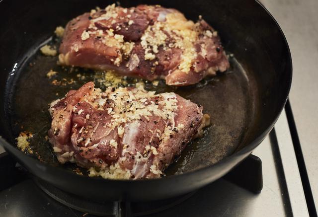 画像: 2フライパンを熱し、オリーブオイルを入れ、1の鶏肉の皮目を下にして焼く。にんにくの半量を鶏肉にのせる。