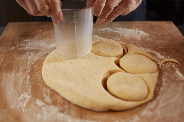 画像: 7 生地をドーナッツ型で抜く。ドーナッツ型がない場合は、写真のようにクリアファイルを切って丸めてセロテープで止めて型を作るとよい。今回は、直径5.5cmと2.5cmになるようにクリアファイルを丸めた。