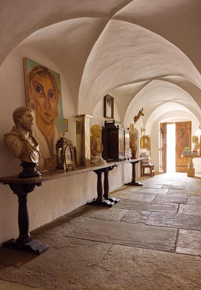 画像: クロス・ヴォールト（註：アーチを交差させた天井）が美しい玄関ホールに飾られているのは、フランチェスコ・クレメンテが描いた、ブラジル人アーティスト、トゥンガの肖像画（2007年）。１～２世紀に作られたローマ皇帝の胸像や、17世紀のフランス製マントルクロック（暖炉を飾る時計）も並んでいる。 PAINTING ON TABLE: FRANCESCO CLEMENTE, “PORTRAIT OF TUNGA,” 2007 © FRANCESCO CLEMENTE,COURTESY OF THE ARTIST AND VITO SCHNABEL GALLERY. PREVIOUS SPREAD