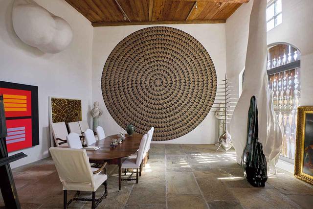 画像: ギャラリーに配された家具は、大きなダイニングテーブルと椅子のみ。作品は左から、ピーター・ハレーの《The Cold Farewell》（2006年）、リチャード・ロングの《Mud Hand Circles》（2007年）、ノット・ヴィタルの《Unpleasant Object》（2008年）、《Tongue》（2001年）、《Tongue》（2008年）など。 PAINTING ON WALL: PETER HALLEY, “THE COLD FAREWELL,” 2006 © PETER HALLEY; PAINTING ON WALL, CENTER: RICHARD LONG, “MUD HAND CIRCLES,” 2007 © 2025 RICHARD LONG, ALL RIGHTS RESERVED, DACS, LONDON/ARS, NY; SCULPTURES, ON FLOOR: NOT VITAL, “UNPLEASANT OBJECT,” 2008, “TONGUE,” 2001 AND “TONGUE,” 2008 © NOT VITAL, COURTESY OF SPERONE WESTWATER.