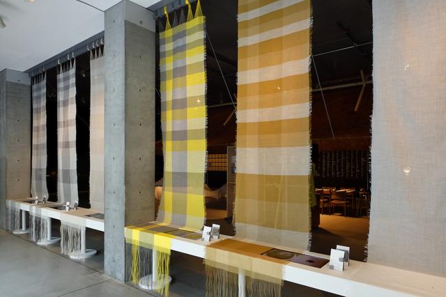 画像: 天井から下がる6枚の布は、縄文時代から用いられてきた天然素材“苧麻（ちょま）”。右から、染められていない布、白、黄、赤、緑、黒の５色の食材で染められた布。布の下に並ぶ画面では、同じ食材を用いて、糸を染めて布をつくる工程とスープをつくっていく様子が並行して映し出される。 『色をまとい、色を味わう ―身体を染める色と味― 』ISSEY MIYAKE＋林 響太朗＋長尾智子 PHOTOGRAPH BY KEIZO KIOKU