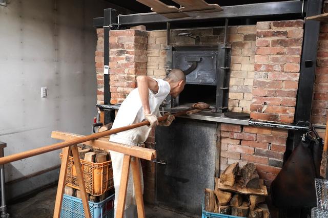 画像: レンガを積み重ねてつくったお手製の薪窯でパンを焼く宙生さん。「日によって、室温や水の温度、窯の温度、薪の乾燥具合、窯の温度の上がり方などが違ってくるので気が抜けない」