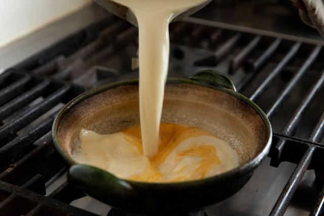 画像: 豆乳を鍋に入れ、弱めの中火にかける。鍋の周りにふつふつと泡が立って煮立ってきたら火を止め、にがりと卵の鍋に一気に注ぎ入れて蓋をし、そのまま3、4分おく。