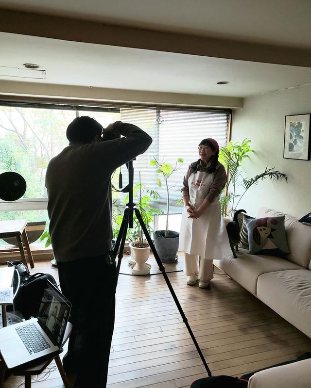 画像: 白地に赤いロゴが映えるエプロンがお似合いの枝元さん。よくみるとねこちゃんが寄り添っています