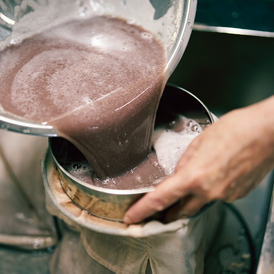 画像: 布袋の口を開け、水に沈んだ小豆の中身をざるでこしながら流し入れる。くだいた小豆もこしながら入れる