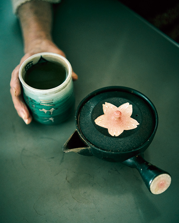 画像: 桜が描かれた急須は五所川原の焼き物。お茶好きのミサオさんが手にする深緑色の湯飲みは長年愛用、孫が旅行先でつくってくれたもの