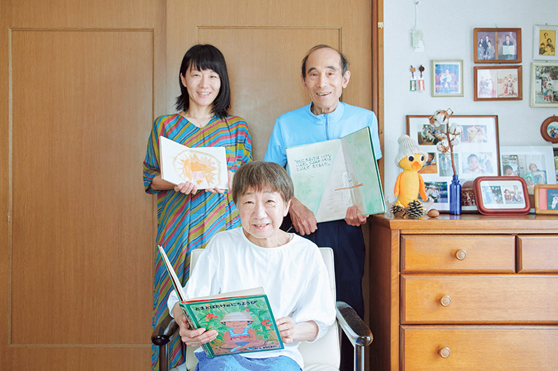 画像: 町田家の母・万里子さん、父・弘さん、長女・はる香さん。長男・穂高さんは関西に。それぞれの手には自作の絵本が。はる香さんのワンピースは「祖母の手縫い」という手仕事好き一家