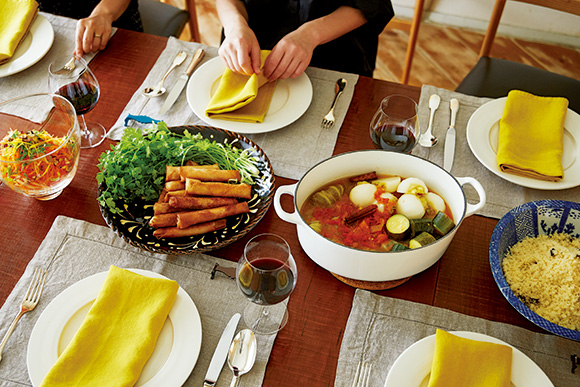 画像: イエローのナプキンをアクセントにして、染め付けやガラスなどいろいろな器を組み合わせたテーブルセッティング。リムの面積が絶妙な白いプレートは、日本の作家さんもの。