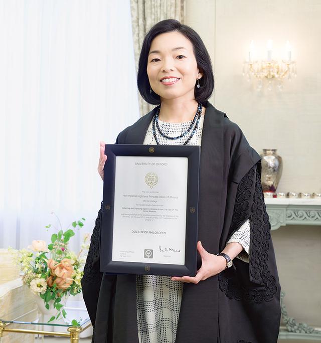 画像: オックスフォード大学の博士課程の修了証書をお手に。黒いガウンは、博士号を取得した人に許されるもの