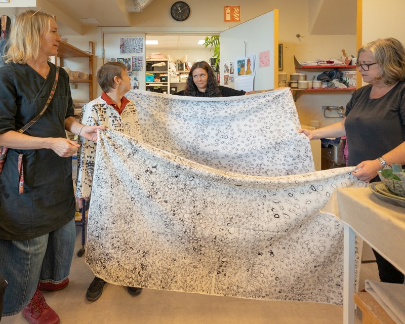 画像: 利用者が持参した自作のテキスタイル。支援員3人がかりで広げる姿に、やさしさがあふれていた