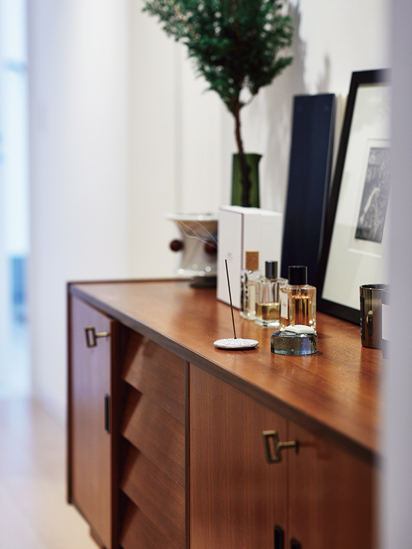 画像: 香水やアートフォト、キャンドルなどがコーディネートされた、玄関前に置かれたビンテージのキャビネット。この上でお香を焚くことが、空間のリセットに