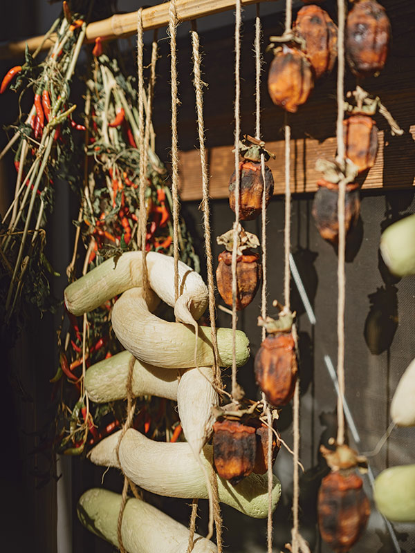 画像: 日当たりのいい軒下に柿と大根を吊るして干す。「大根は毎年収穫したうちの半量を干してたくあんにします」。それでも余った野菜はご近所に配る