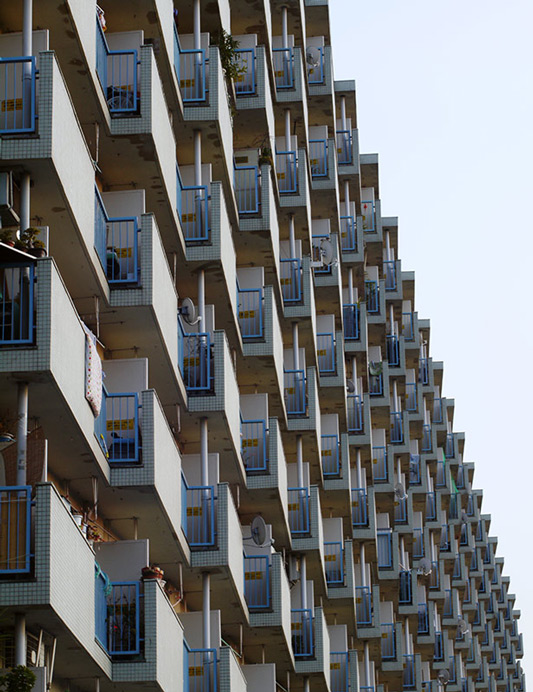 画像: こちらは、少しでも採光を入れようと、各住戸が南側に壁とベランダを傾けたタイプの団地です。この連続感がたまりません