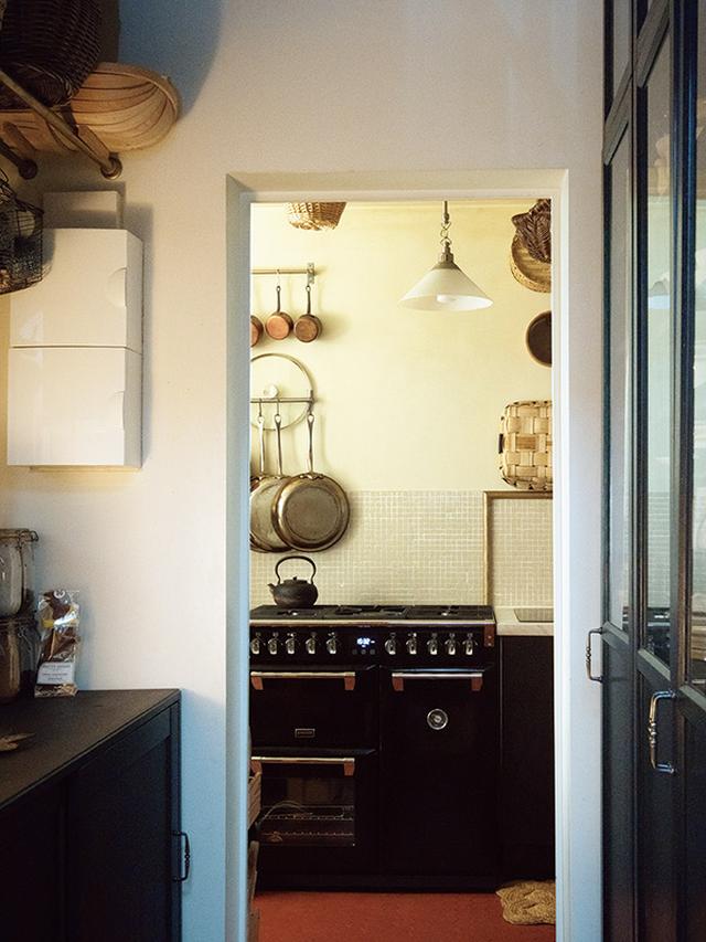 画像: 床の古いレンガは蜂の巣形でお気に入り。ダイニングに続く廊下には食器棚を置いて。「ここも台所の一部です」