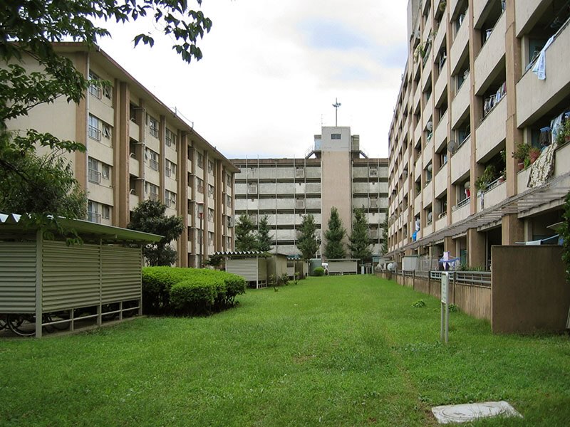 画像: 21号棟通路側はこんな感じ(写真奥)。階高が低い上に、安全対策のためかプライバシー保護のためか分かりませんが、手すりが異様に高く、装甲に守られた軍艦やお城のような重厚感がありました。夏は玄関ドアを少し開けて室内に風を通すお宅もあったようですが、このコンクリートの手すりでは、あまり風が通らなかったかもしれませんね