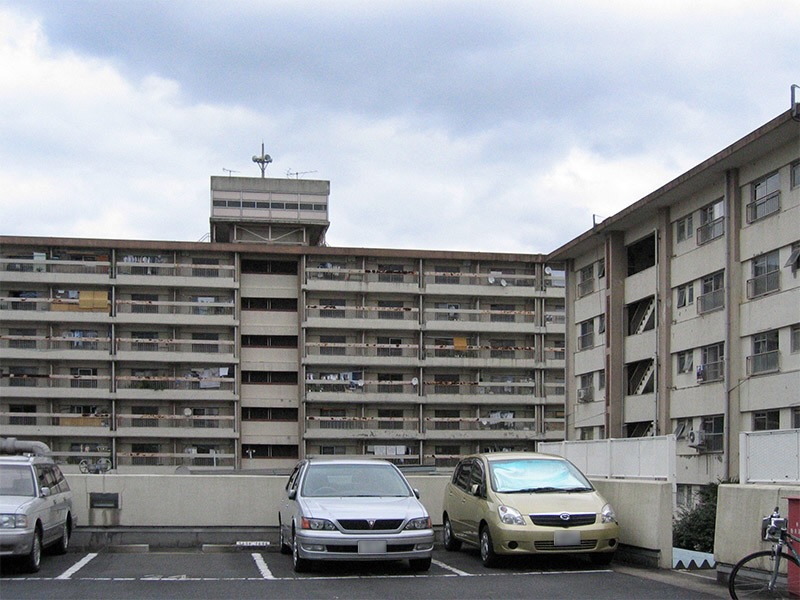 画像: 21号棟は当時としては珍しい7階建ての住棟です。エレベーターが完備されていました。天井高が低く7階建ての割りには建物の高さはそれほど高くありませんでした。屋上のエレベータの機械室か給水タンクと思われる屋上の展望室のような部分、一度登ってみたかったです。右下にちらっと写っている自転車が、当時団地巡りに愛用していたクロスバイクです。これで、遠くの団地にも出かけてました