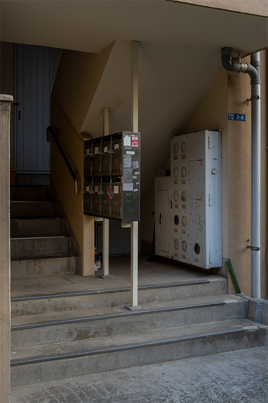 画像: 赤羽台団地では逆に珍しい気もする、後にスタンダートとなった縦階段の「板状階段室型住宅」。とはいえ、ど真ん中に浮かせる配置になっているポストが斬新です。丸窓の配電盤?はこの時代の団地でよく見られました