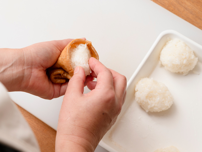 画像: 油揚げの口を開き、破れないように丸めた酢飯を奥まで入れ、端を折りたたんで口を閉じる