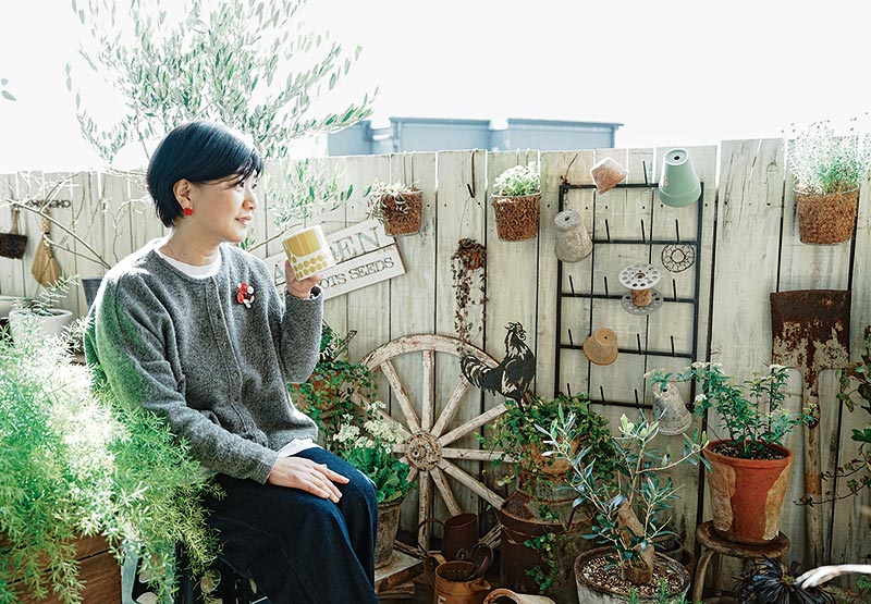 画像: 花台にしているスツールに腰かけて。植物を眺めているうちに模様替えのアイデアがわいてきて、気がつけば掃除に突入していることもあるとか