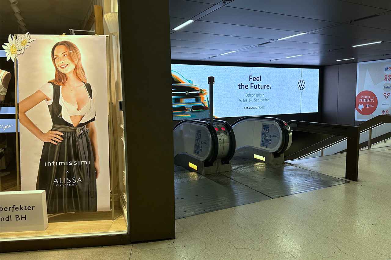 画像: Uバーン(地下鉄)駅にて。オクトーバーフェストを前にしたイタリア系ランジェリー・ショップのディスプレイと、可変広告に映ったVWパビリオンの告知。祝祭は続く。