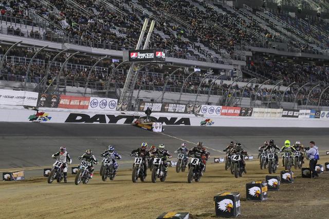 画像: トップカテゴリーAFTツインズの決勝25LAPSスタートシーン。スーパースピードウェイ・トライオーバル中央のフィニッシュライン付近が本戦でもスタート/フィニッシュラインとなる。先週の当コラムで解説した、オーバルトラック走法の基本原則を飛び越えて "フロントブレーキとシフトチェンジがなければ曲がりきれない" ターン1を目がけて、6台 x3列でスタートした18台が一斉に加速する。 www.americanflattrack.com