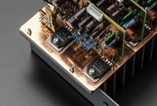 画像: パワーアンプ部の出力素子には、サンケン電気との共同製作によるDHCT(Denon High Current Transistor)を搭載。アイドリング精度を向上させるためにアイドリング電流補償用のデバイスを内蔵しており、瞬時の大電流出力にも安定して応えられるという。さらに発熱対策として、ヒートシンクの裏側(写真で見えている部分)には銅板を使って熱を逃している。これは同社の2chオーディオ製品でも使われる手法で、AVセンターでは初採用だ