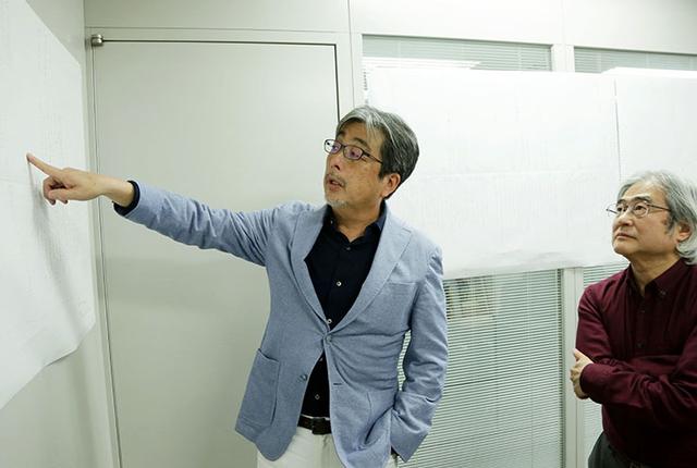 画像: 壁に貼られた35年分のハード年表を見ながら、画質について話しをする山本さん(左)と吉田さん(右)