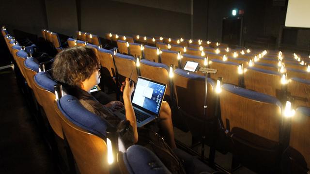 画像: 音響チェックを行なう岩浪さん。手に持っているのはトランシーバーで、上映室にいるスタッフとやりとりをしている