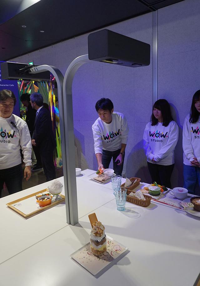 画像: インタラクティブ・キャラクター・カフェでは、出された料理に応じて様々なアニメーションが再生される。上の写真でコーヒーカップの周りに投影されているのがうさまるのアニメだ。料理の検出と映像投写はテーブルの上に設置されたセンサー付きプロジェクターで行なう