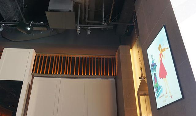 画像: 写真左上、ライティングレールに取り付けられている円柱状の物体がプロジェクターのEV-105。ここから右側のスクリーンに映像を再生している。レーザー光源なので、色再現もとても綺麗だ