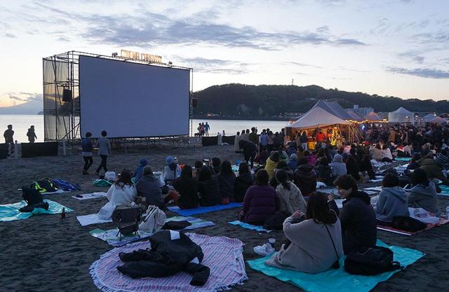 画像: 波打ち際にセットされた大型スクリーンに映画が上映される。日が沈む頃には夕焼けをバックに幻想的な風景が広がる