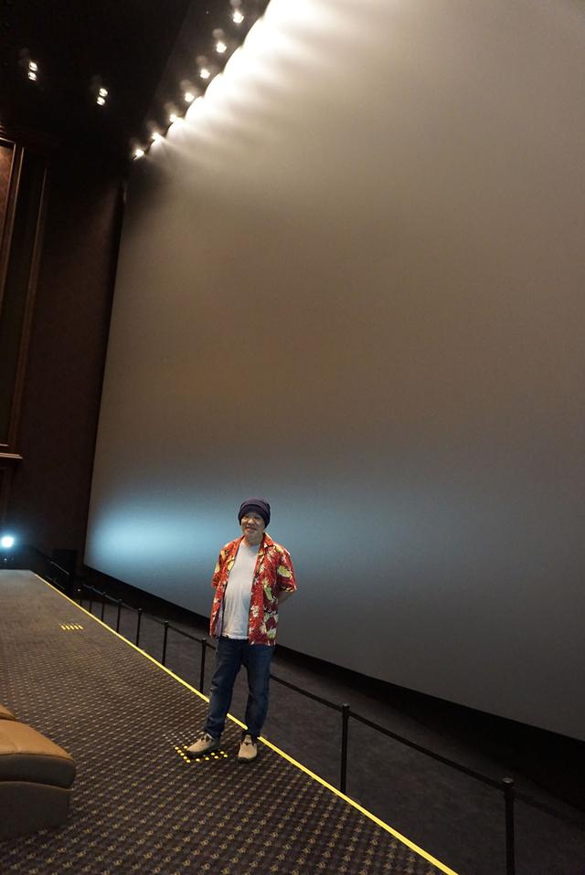 画像: スクリーン前に立つ久保田さん。高さは18.9mで、通常のビル6階分に相当する。写真からその巨大さがわかるだろうか