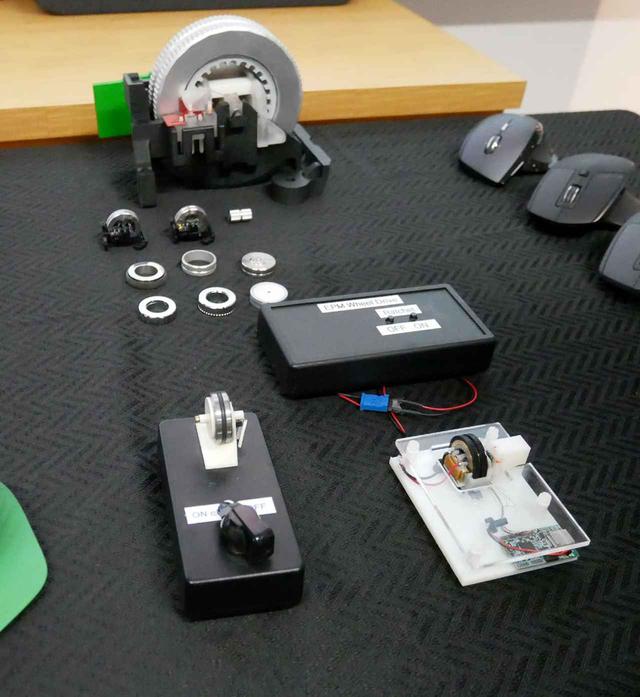 画像: 電磁ホイールの各種試作機。手前右が1号機。同左の箱状のものが2号機。奥にあるのが電磁ホイールの拡大模型