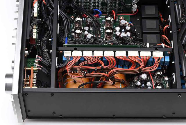画像: 本機の最大の特徴はLECUTAと名付けられた電子制御トランス式アッテネーターの搭載。34タップのファインメット・コア・トランス(写真手前)と対を成す34個のリレー(写真のトランスの奥)を位置情報検出用ボリュウムノブ(左、フロントパネルに設置)で切り替えるという設計で、ボリュウム自体には音楽信号が流れない方式。