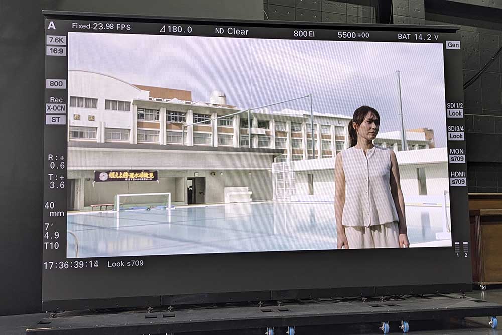 画像: 実際に撮影したものを大型モニターに出力。全く違和感なく背景に溶け込んでいる