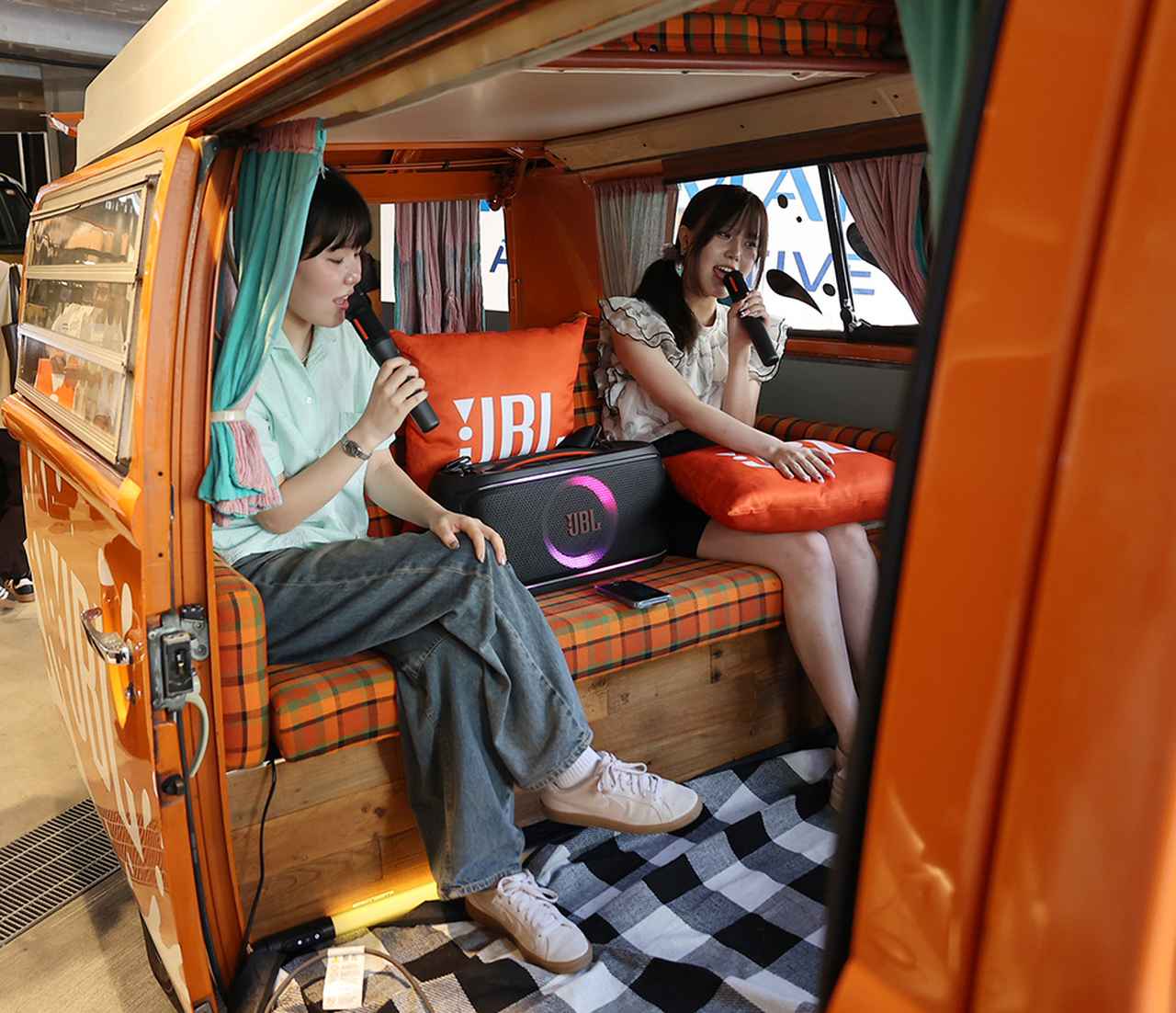 画像: アメリカンサイズのラジカセ、といった風情のパーティースピーカー「JBL PartyBox On-The-Go 2」を車内に持ち込んで、カラオケを楽しむスタッフ。マイクが2本ついているので、いつでもどこでも楽しめますよ、のデモ